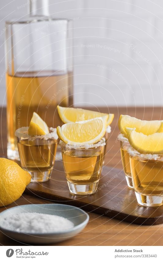 Tequila in shots with salt rim and lemon alcohol tequila booze table wooden glass beverage drink fresh tasty citrus orange party delicious yellow organic food