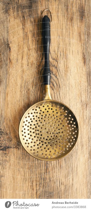 Old skimmer on rustic wood used brass retro wood - material retro style work tool one single shiny empty mesh strainer closeup domestic old kitchenware