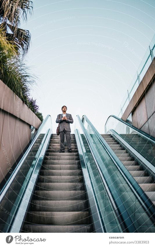 Businessman in a suit drinking a coffee and riding up an escalator adult airport attractive boss business business people business wear businessman