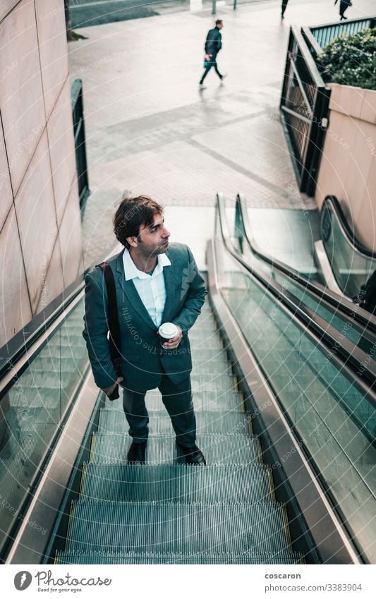 Businessman in a suit drinking a coffee and riding up an escalator adult airport attractive boss business business people business wear businessman