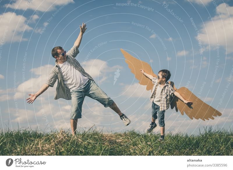 Father and son playing with cardboard toy wings father child outdoor family people parent lifestyle together fun day kid boy summer happiness dad man young joy