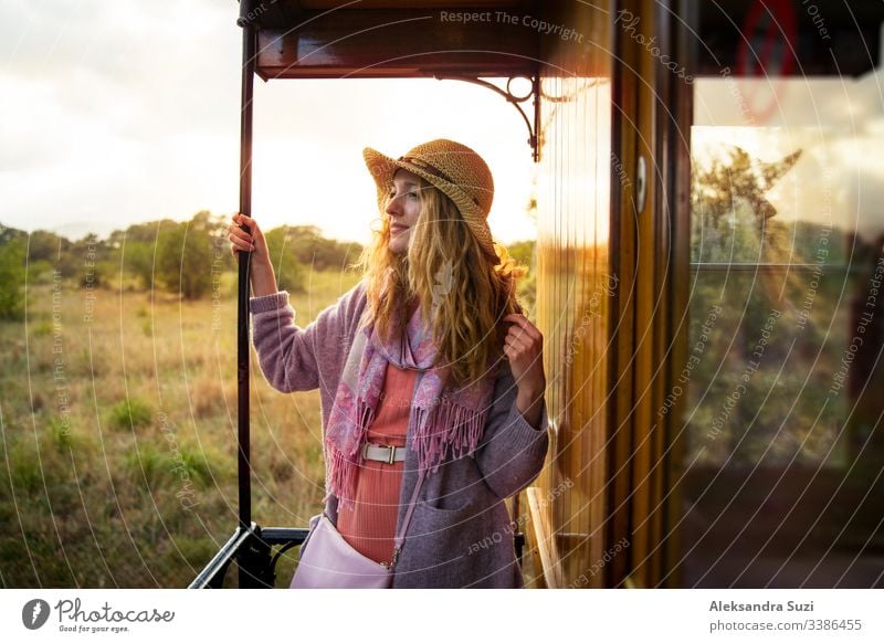 Young woman in straw hat traveling by retro wooden train. Sunset landscape, wind in blond hair. Girl smiling happily. Majorca, Spain. adventure beautiful
