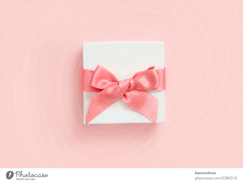 White gift box with a bow on a light pink background white ribbon love romantic top view above present concept creative day decor decoration design floral