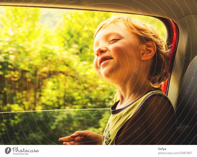 Little caucasian boy enjoying sun and wind travelling in a car with open window. little child happy skin emotion moment hair summer sunny day light t-shirt
