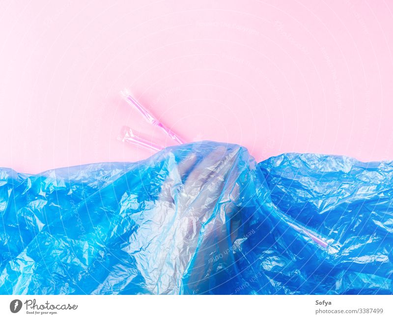 Plastic straws being thrown in ocean represented by blue plastic bag and hand under water. Pollution concept on pink background. pollution metaphor sea flat lay
