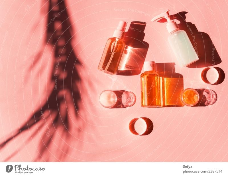 Various cosmetic products in bottles and mini jars on pink coral. Flat lay shot in hard light with plant shadow. skin flat lay orange cream care golden yellow