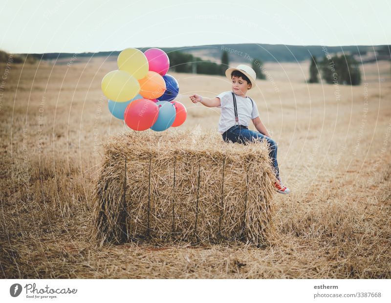 happy child with balloons in the field adventure discover freedom grain grass growth happiness hat independence joy lifestyle multicolored outdoors party play