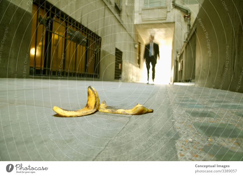 Low angle view of a businessman walking towards a banana skin accident be careful careless carelessness caution concept conceptual danger dangerous foot hazard