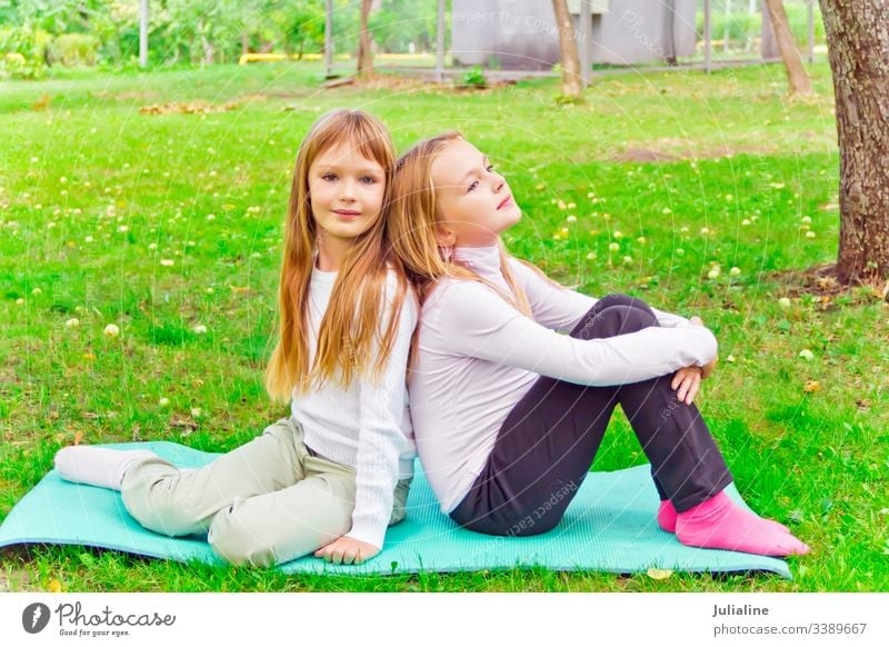 Two seven years old girls sitting on green grass sister play two female lifestyles leisure activity recreational child kid smiling preschooler schoolgirl six