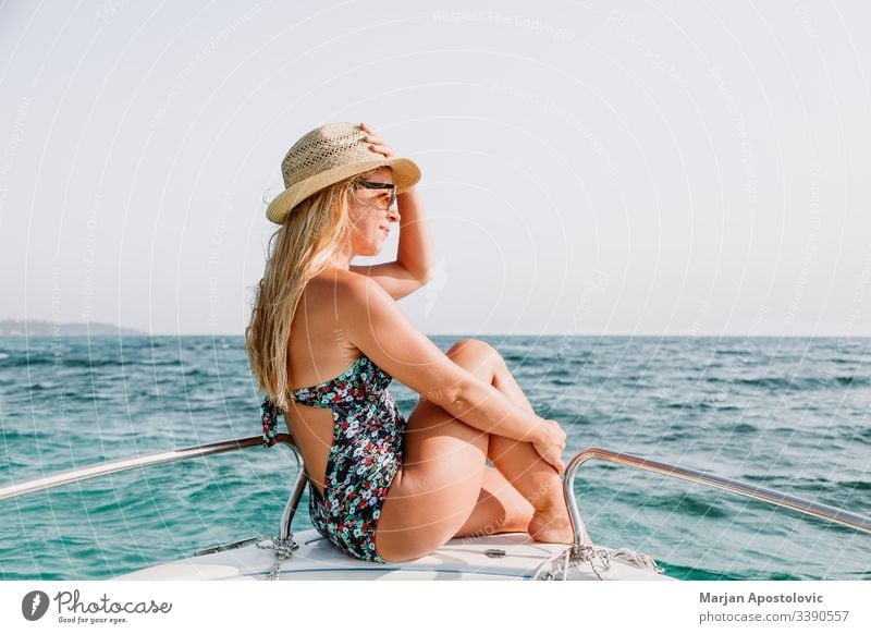 Young woman enjoying on deck of a boat on the sea young ocean water cruise leisure relaxing vacation summer holiday travel tourism sunbathing bow hat blonde