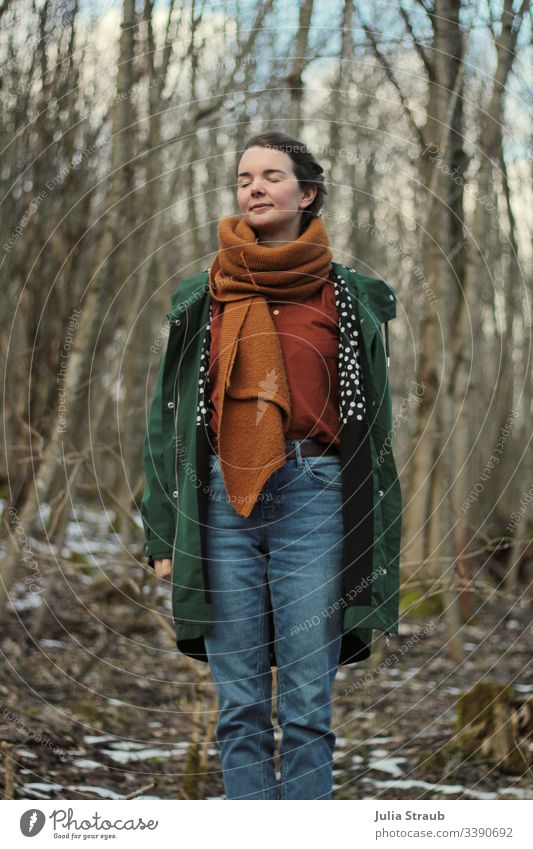 Woman standing in the forest with closed eyes Forest trees Clouds Coat Scarf shirt blouse Jeans Spotted Breathe Closed eyes Belt ochre Green Exterior shot