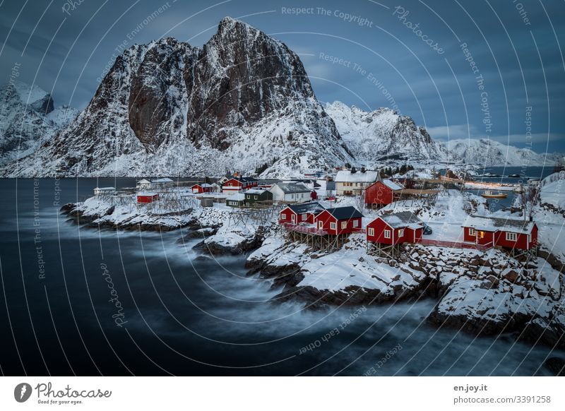 Fisherman's cabins on island in the fjord on rocks with snow in front of mountains with cloudy skies has given us a home for a few wonderful days Motion blur