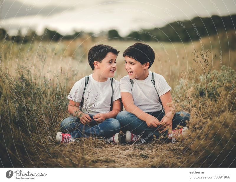 smiling brothers sitting in the field children boys twins conversation siblings family union lifestyle complicity friends smile smiles friendship fun game grass