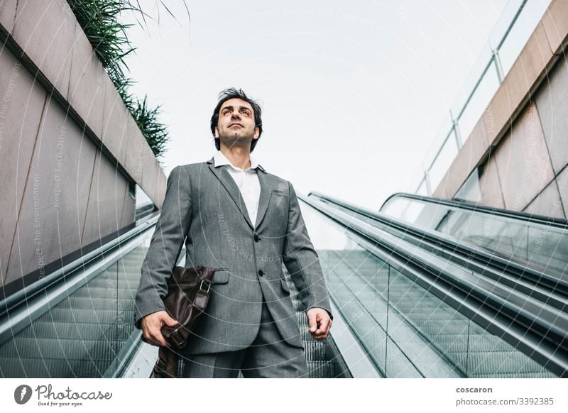 Businessman in a suit riding up an escalator adult airport attractive boss business business people business wear businessman businesspeople city coffee