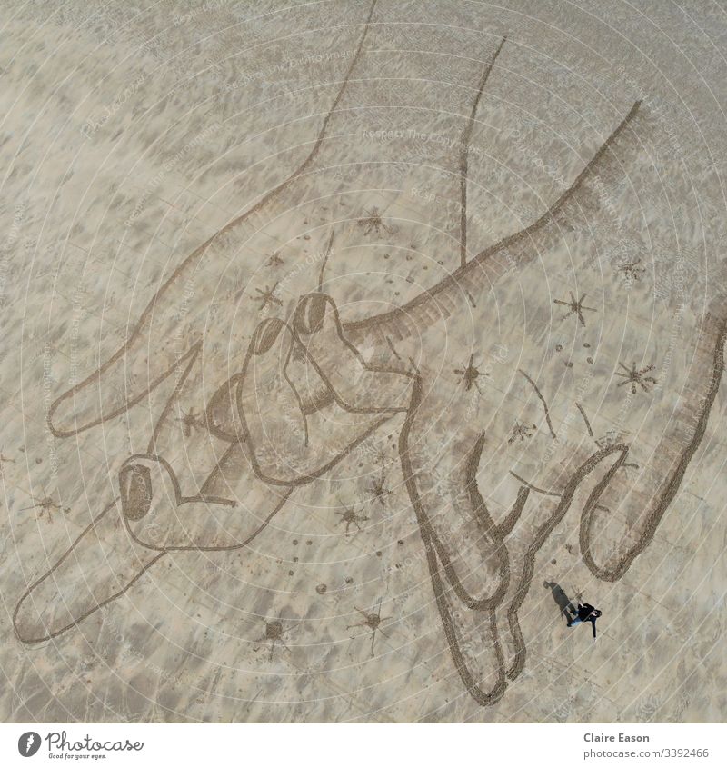 Giant sand art drawing of hand holding with a person for scale; created by dji camera hands holding hands romance nature environment coast beach clean