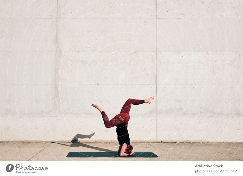 Woman doing balance exercise in headstand with split pose while practicing yoga on street woman acrobatic practice training urban sirsasana concrete strong
