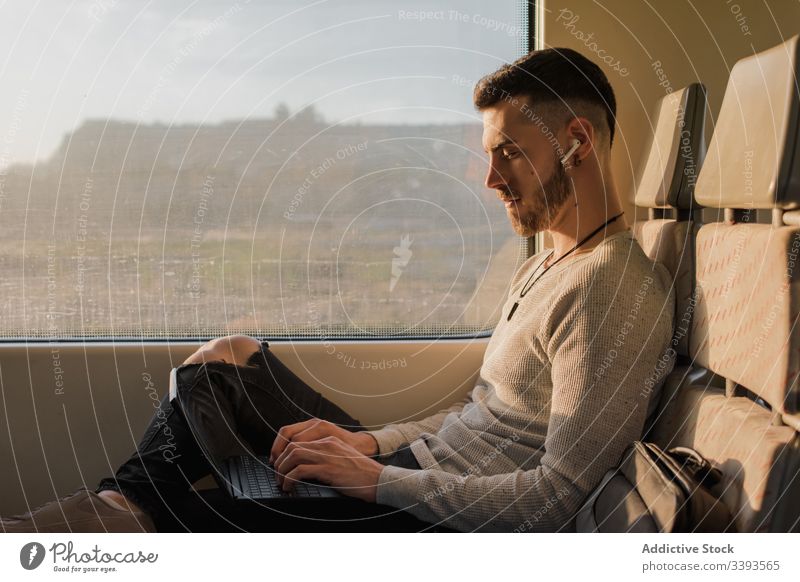 Concentrated male passenger using laptop in train man wireless earphones typing journey subway sunny communication connection contact information surfing