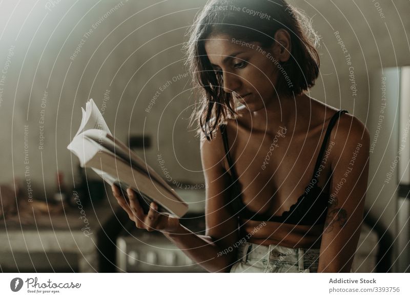 Concentrated young female reading book in kitchen woman enjoy interested comfort pleasure information literature knowledge education domestic hobby bra idyllic