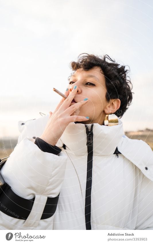 Stylish ethnic female teenager with cigarette woman smoke cool nature warm clothes blunt nicotine provocative casual young style jacket hipster accessory