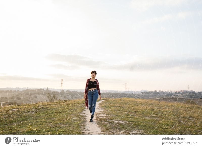 Female hipster in trendy outfit on empty rural road woman casual nature teen suburb field countryside grass sky lifestyle young cloudy walk meadow teenager rest