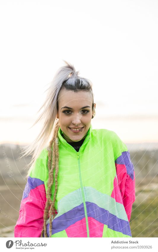 Young woman with modern hairstyle in colorful sportswear teenage hipster extraordinary pensive cool nature jacket dyed hair contemporary female sky sunset