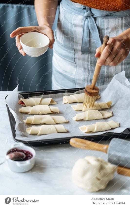 Cook holding bowl and brushing croissants in baking sheet on table cook jam dough preparation sliced bakery homemade culinary making sweet raw dessert recipe