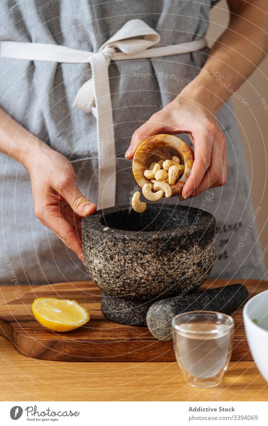 Woman adding cashews to mortar woman cook healthy kitchen dish food preparation home meal ingredient culinary cuisine organic natural recipe dinner lunch