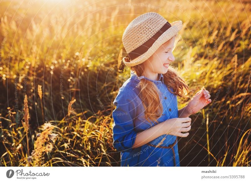 happy kid girl in blue dress and straw walking on summer sunny meadow. Lifestyle shot, rural living and summer traveling concept child nature lifestyle