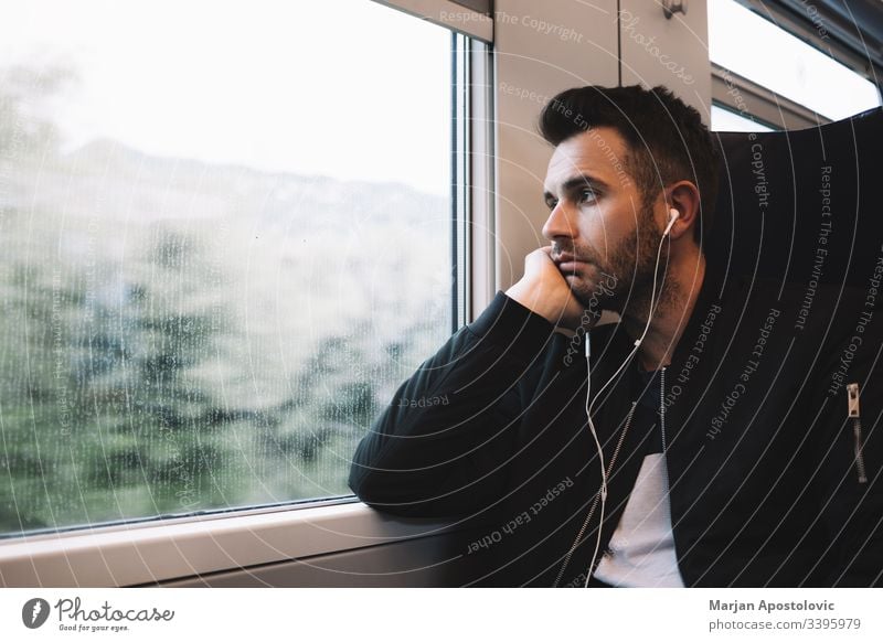 Young man traveling by train wearing earphones 30s adult alone bearded casual caucasian commute commuter day everyday guy handsome headphones journey life