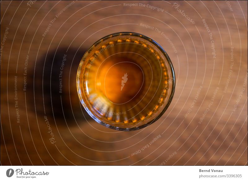 Drinking glass from above Glass Wooden table blurred edge at home Beverage drinking glass Close-up Fluid Alcoholic drinks Colour photo Yellow Artificial light
