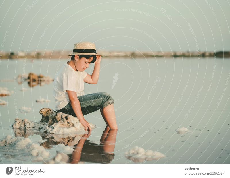sad and pensive boy sitting on the beach child childhood nostalgic thoughtful Thought loneliness lonely expression freedom innocence portrait serious dream sea