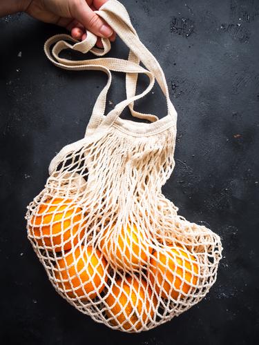 Hand mit einer wiederverwendbaren Einkaufstasche und frischen Orangen auf einem schwarzen Hintergrund einkaufstasche halten Healthy Eating Fruit Food Vitamin