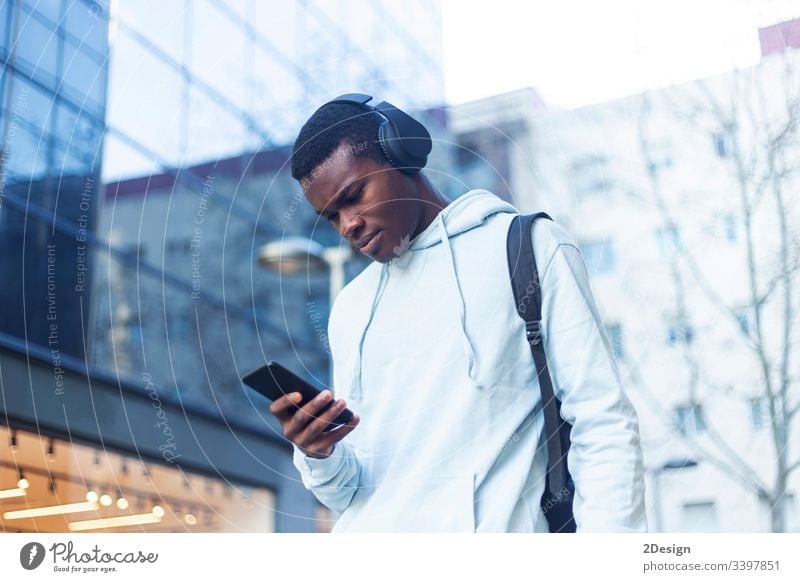 Young Black man standing in the street while listening music by headphones technology lifestyle male black casual attire trendy happy african earphones guy