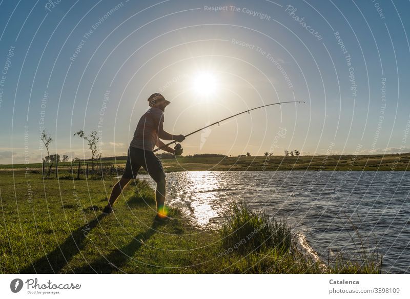 Young man fishing on the lake, the sun is low, the wind has died down, the fish should bite Nature Environment flora Plant Meadow Grass Water Body of water Lake