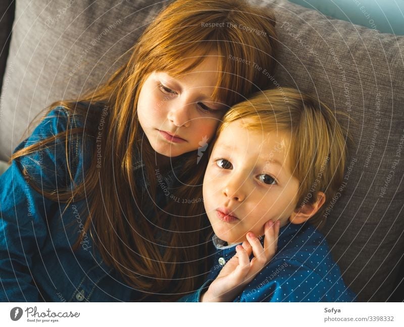 Two blonde little sibling kids on a sofa child smile face hug family love siblings brother sister redhead funny sweet tender together near indoors portrait