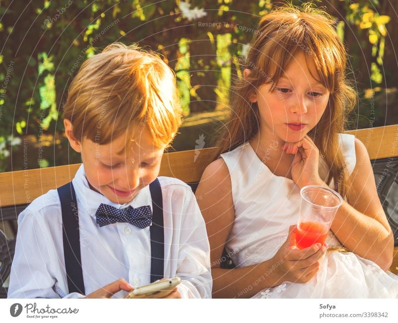 Ring bearer and flower girl relaxing at wedding children technology using smartphone boy happy mobile hang out break ring bearer summer siblings play kid nature