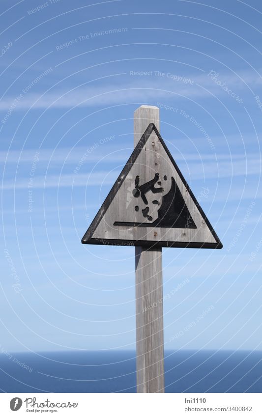 Beware of cliffs! Danger of falling! Wooden shield in front of a blue sky and with view to the sea Risk of collapse steep coast Danger of Life Wooden sign