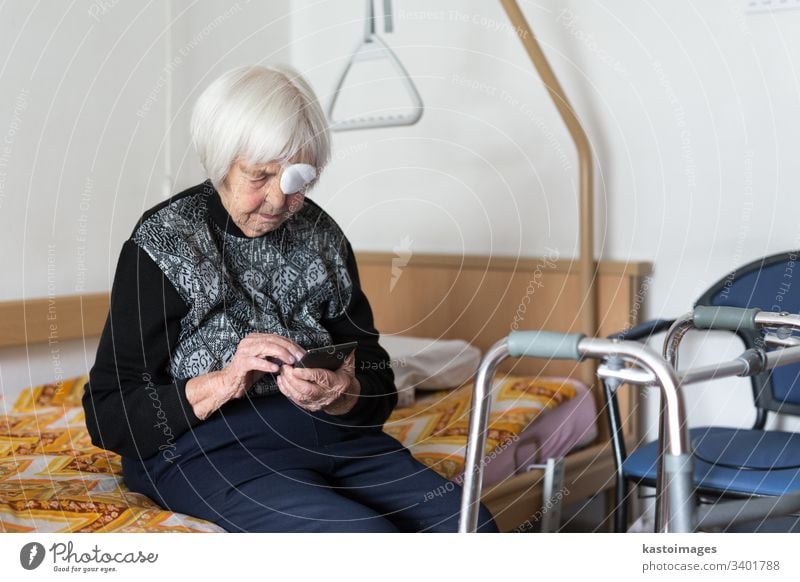 Lonley elderly 95 years old woman sitting at the bad using modern mobile phone. senior pensioner care disability hospital mobility home citizen clinic retiree
