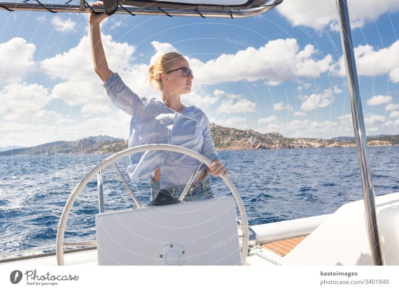 Attractive blond female skipper navigating the fancy catamaran sailboat on sunny summer day on calm blue sea water. nautical steering wheel sailing boat woman