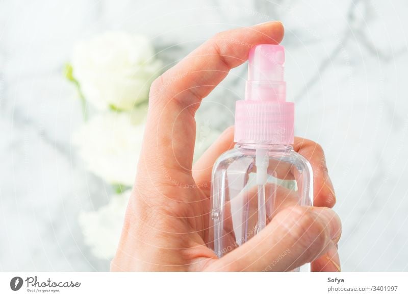 Woman's hand spritzing liquid from spray over marble background with white flowers bottle small pink hair product beauty care cosmetics tonic face push use