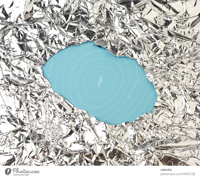 texture of shiny crumpled piece of foil with a hole in the middle, packaging material for food folded gloss glossy gray grey grunge industrial industry light