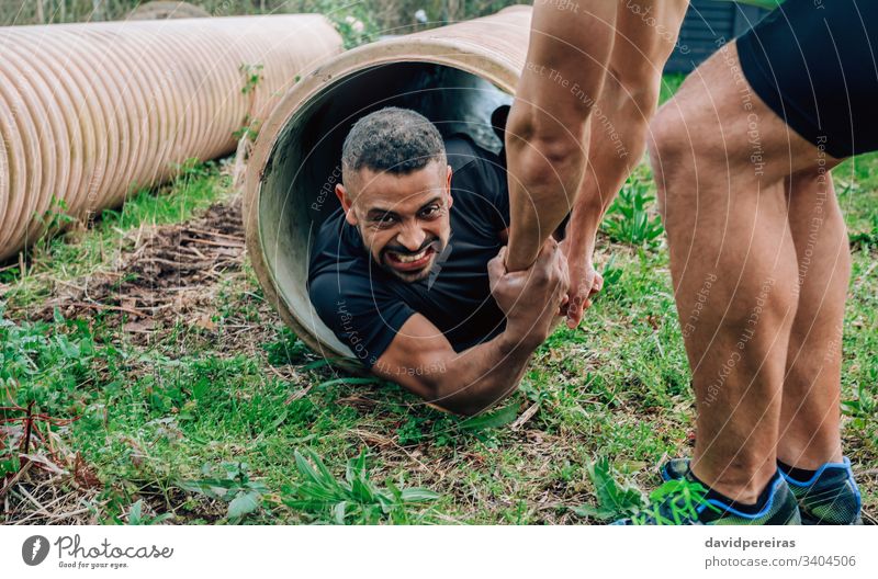 Participants obstacle course going through a pipe effort grimace obstacle course race men mulatto tube crawl helping team spirit overcoming exertion man