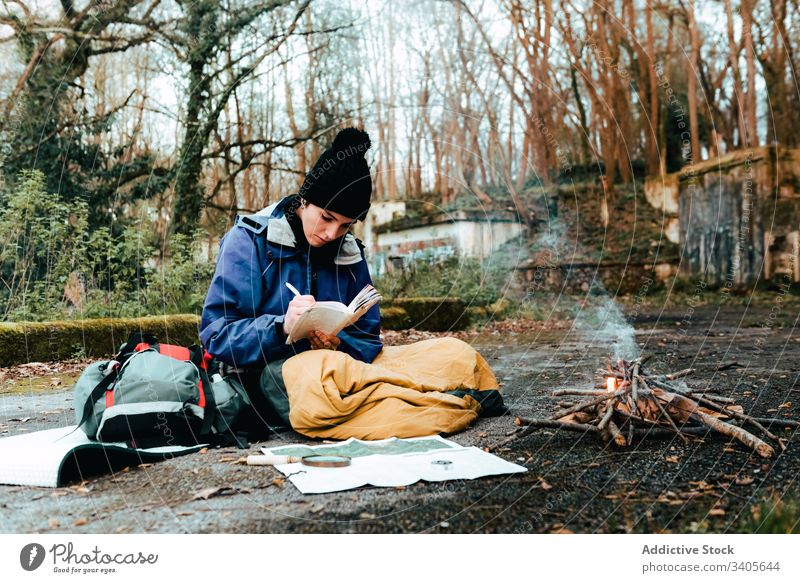 Young female backpacker making notes at campfire woman hiker write information trekking route rest bonfire countryside autumn nature environment adventure