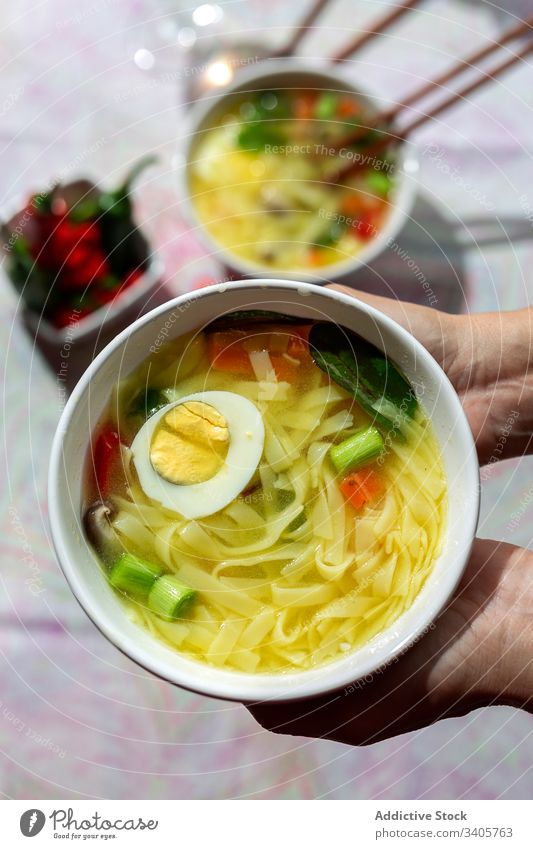 Anonymous person holding a bowl of noodles soup in a restaurant food ramen asian chinese vegan food vegetables vegetarian healthy food egg carrots onion spinach
