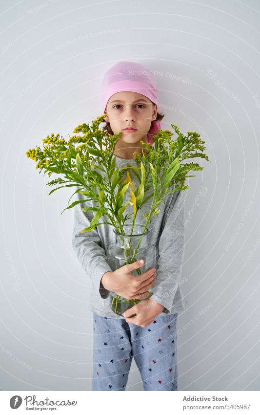 Serious cute child with flowers at wall cancer diagnosis vase plant boy sick fight small male patient courageous disease against awareness recovery strength kid