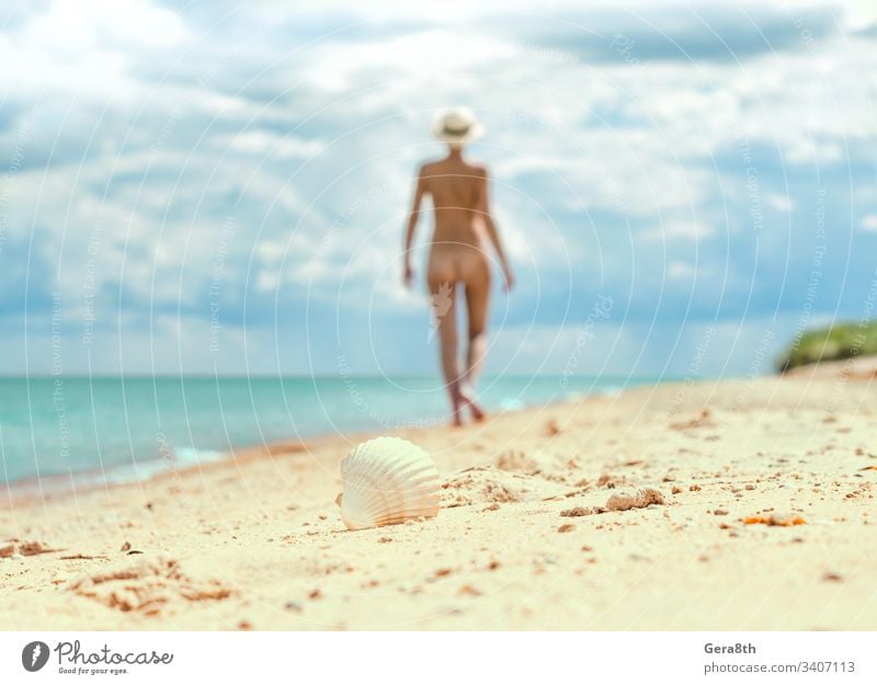 young nude girl with a hat walks on an empty beach near the sea surf against the blue sky with clouds in summer alone blur body climate day erotic female figure