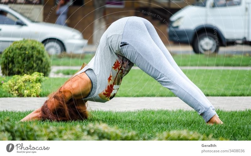 young girl in yoga pose on green grass on lawn on city street background adult bright bushes cars day exercise feet hair hands head houses park performance