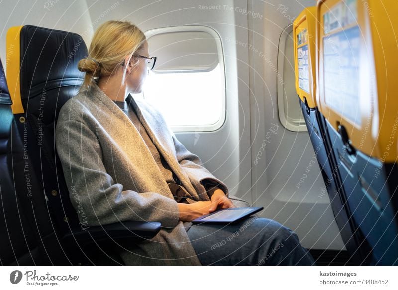 Thoughtful woman looking through the window while traveling by airplane. seat cabin flight inside aircraft passenger e-reader thoughtful economy trip airline