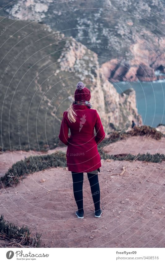 Young woman on a red coat contemplating the sea from the top of a cliff one standing atlantic water scenic landmark edge marin light space Sintra safety beauty