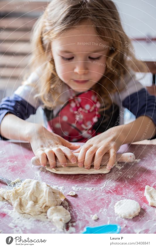 Beautiful blonde little girl playing with dough beautiful curly hair baking cooking rolling pin close up hands sweets delicious home-made cute adorable